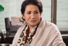 لقطة مقربة للفنانة سعاد عبد الله بابتسامة هادئة، مع خلفية ضبابية لعلم الكويت، تعبيراً عن حالة الجدل حول أنباء سحب الجنسية من الفنانة سعاد عبد الله.