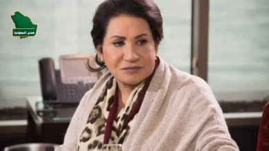 لقطة مقربة للفنانة سعاد عبد الله بابتسامة هادئة، مع خلفية ضبابية لعلم الكويت، تعبيراً عن حالة الجدل حول أنباء سحب الجنسية من الفنانة سعاد عبد الله.