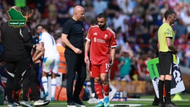 محمد صلاح واقفا على أرض الملعب بقميص ليفربول وهو يمسك ساقه متألماً، بينما يحيط به الجهاز الطبي لتقييم إصابة صلاح.