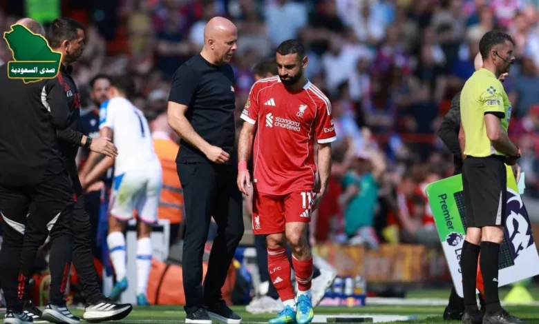 محمد صلاح واقفا على أرض الملعب بقميص ليفربول وهو يمسك ساقه متألماً، بينما يحيط به الجهاز الطبي لتقييم إصابة صلاح.